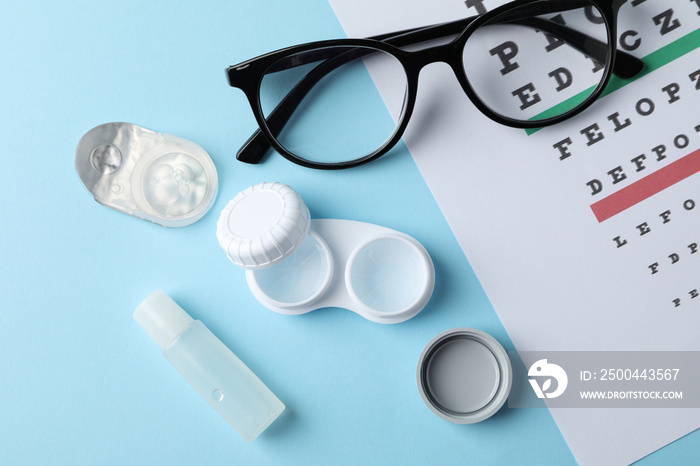 Glasses, contact lenses and eye test chart on blue background, top view