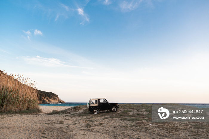 Full length old vintage off-road car parked on the ground with beautiful sandy beach on background. 