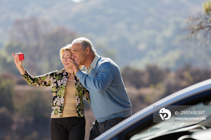 Happy senior couple video chatting outside car at sunny roadside