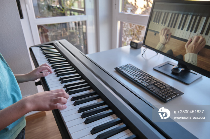 男孩用电脑观看钢琴教程视频。一个人用在线课程练习演奏