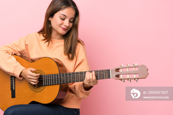 Young brunette girl with guitar over isolated pink background