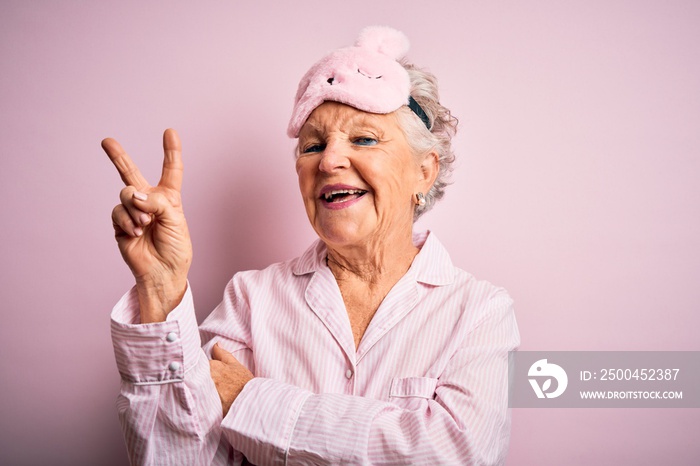 Senior beautiful woman wearing sleep mask and pajama over isolated pink background smiling with happ