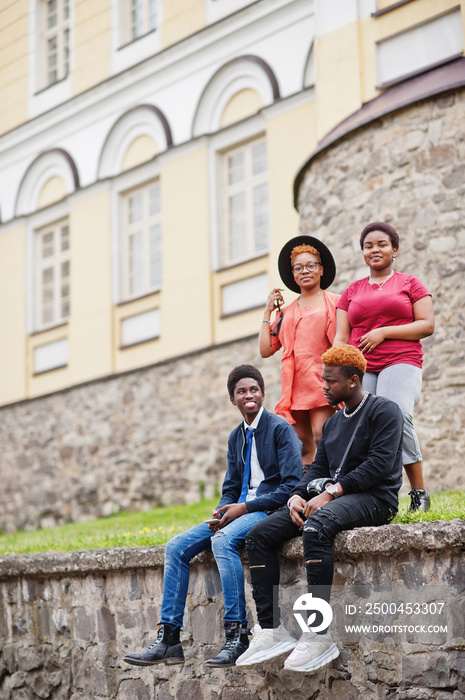 Four african friends having fun outdoors. Two black girls with guys sit an old city.