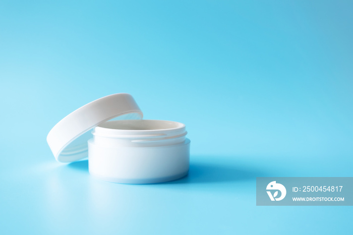 Open moisturizer cream in white plastic jar on blue background, front view. Luxury mockup cosmetic b