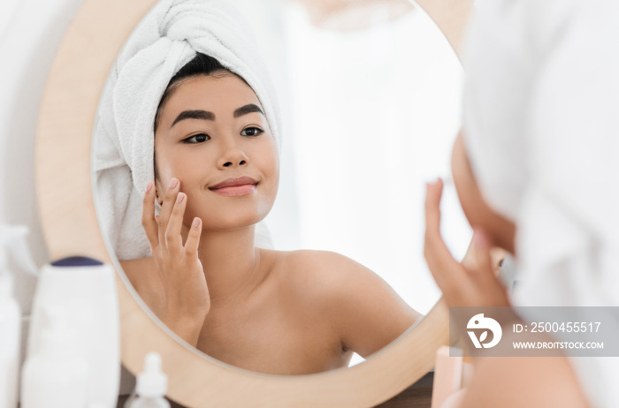 Cheerful asian young woman applying face cream