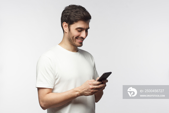 Side portrait of handsome man, isolated on gray background, looking down at smartphone screen, excha