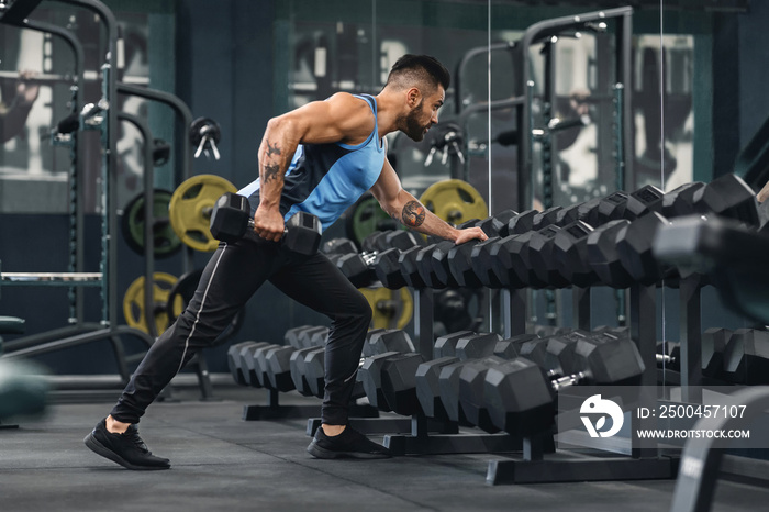 Young bodybuilder taking dumbbells from equipment rack at gym