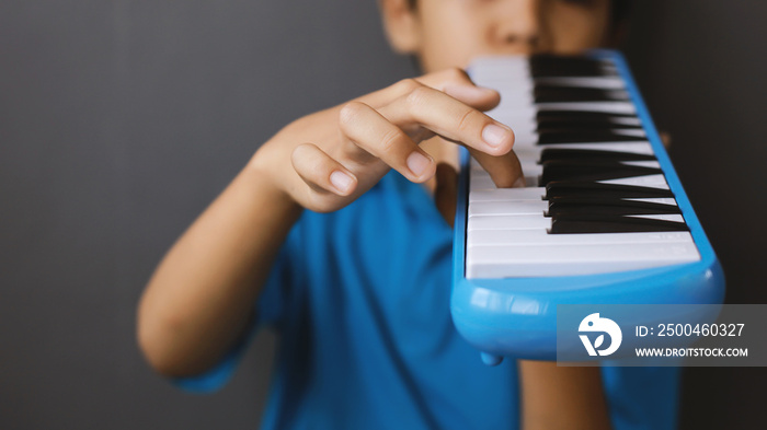 Boy playing blue melodeon musical instrument, melodica blow organ, pianica or melodion in dark gray 