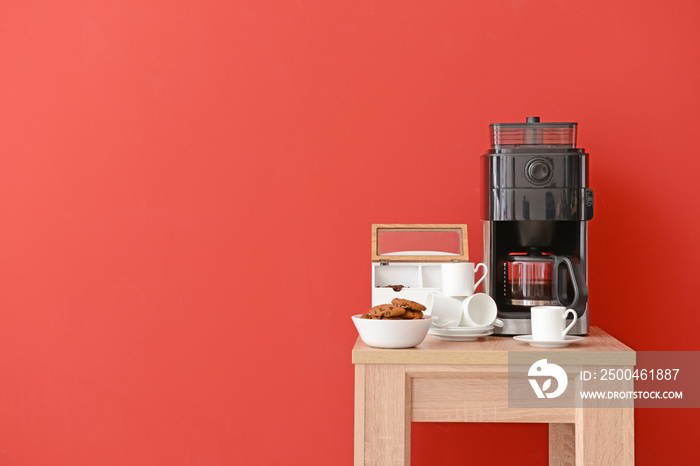 Modern coffee machine, cups and cookies on table against color background