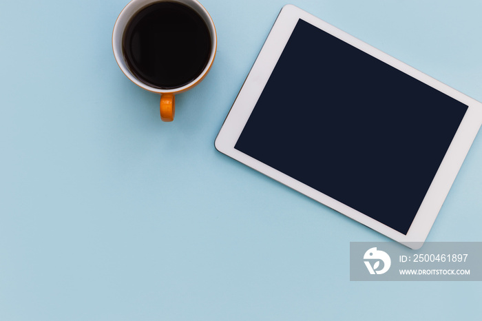 White tablet computer with coffee cup on blue color background