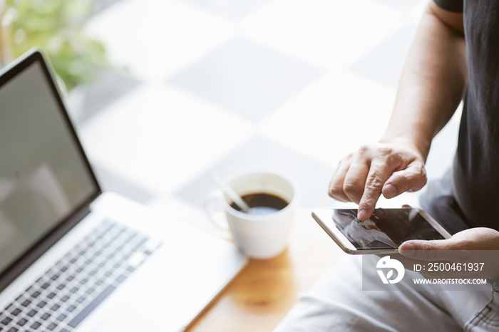 Smartphone in young man hand with blur laptop and coffee background , selective focusing .