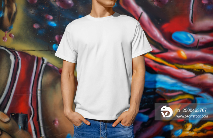 Template of a white T-shirt on a guy, against the background of a colorful wall, front view.