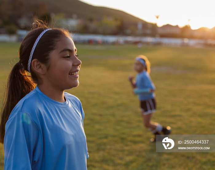 Smiling girl looking away while standing on soccer field against clear sky during sunset