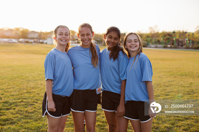 Portrait of smiling friends standing on soccer field against clear sky during sunset