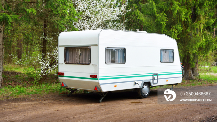 White caravan trailer in a green forest, sunny spring day. Transportation, road trip, vacations, tou