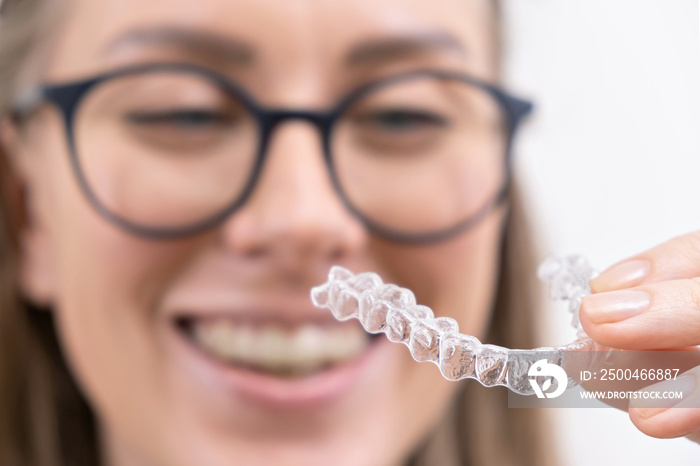 smiling woman using clear plastic removable braces aligner or whitening tray. dental orthodontic car