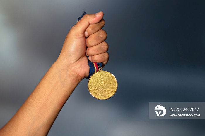 Hand holding gold medal on against cloudy sky background