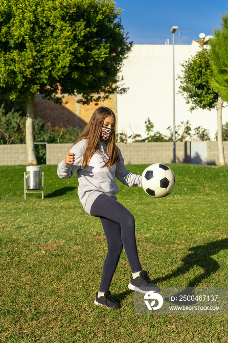 美丽的小女孩在一个阳光明媚的冬日，在一个有天然草地的漂亮公园里踢足球。收到