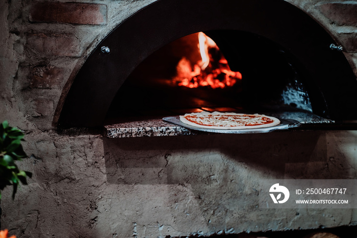 意大利厨师正在把准备好的玛格丽塔披萨放进烤箱，烤箱里有火焰。
