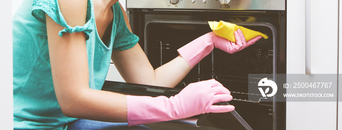 Young woman cleaning oven in the kitchen