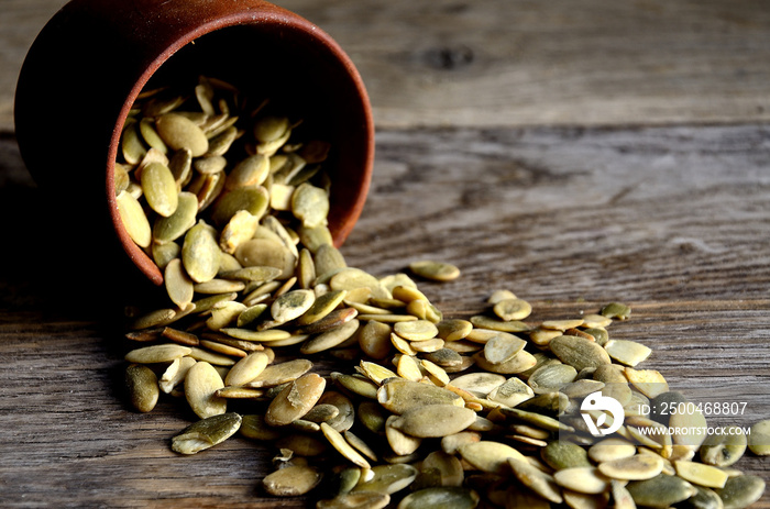 Peeled pumpkin seeds are scattered from wooden dishes on a wooden table ..