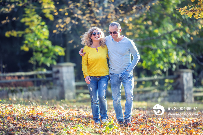 Happy mature couple in autumn park in the embrace walk on the fallen maple leaves