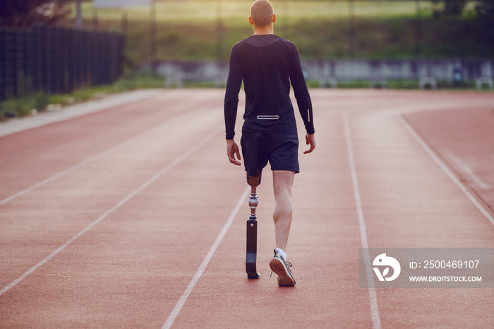 Rear view of handsome caucasian handicapped young man with artificial leg and dressed in shorts and 