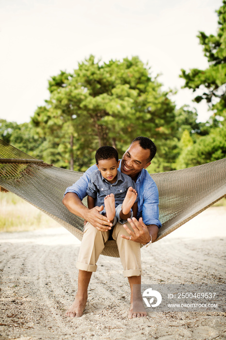 Smiling father with his son sitting on hammock outdoors
