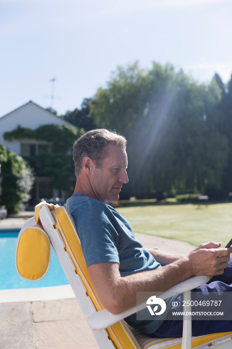 Mature man using smart phone at sunny poolside