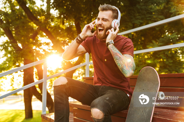 Attractive cheerful young man sitting at the skate park ramp