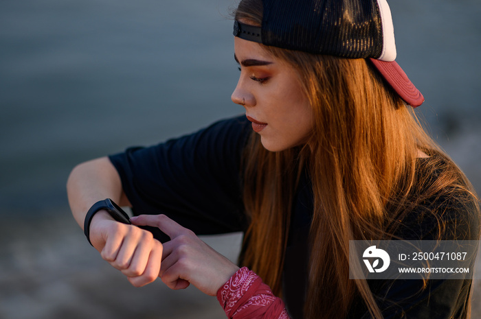 Young woman sitting near the river and checking her smartwatch