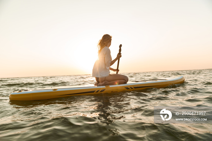 Beautiful young woman sitting on a stand up paddle board