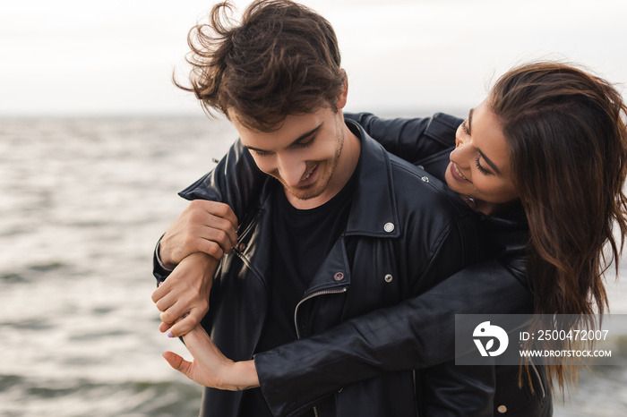 Brunette woman hugging boyfriend in leather jacket near sea