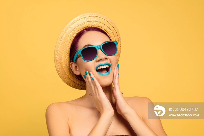 Portrait of beautiful woman with bright make-up, hat and sunglasses on yellow studio background. Sty