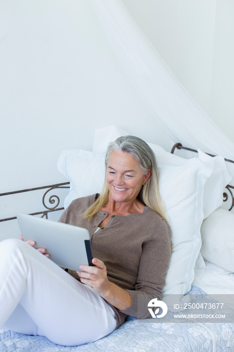 Smiling senior woman relaxing with digital tablet on daybed