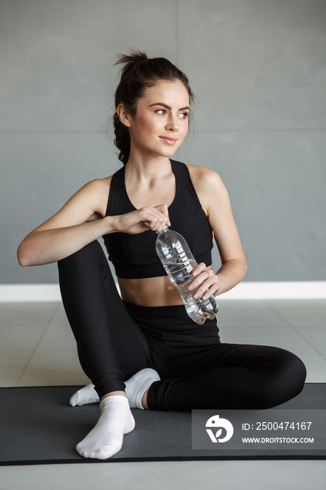 Photo of pleased brunette woman drinking water while working out