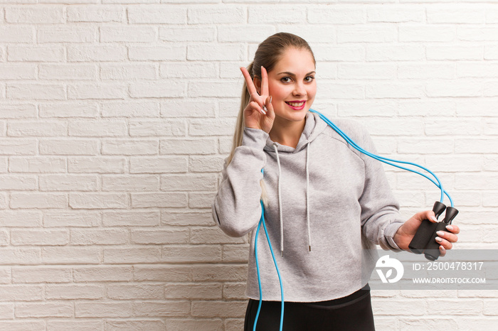 Young fitness russian woman holding a jump rope against a bricks wall