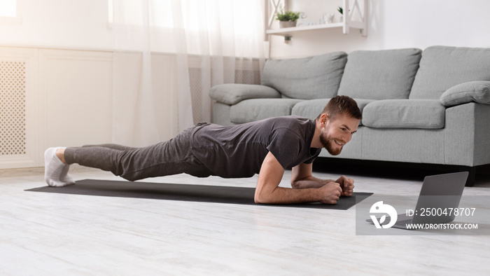 Young man doing plank exercise with online tutorial at home