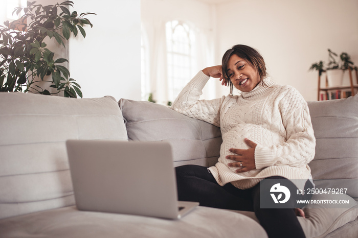 快乐的孕妇坐在沙发上用笔记本电脑