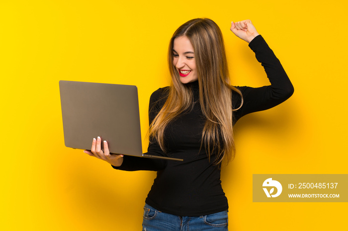 Young pretty woman over yellow background with laptop and celebrating a victory