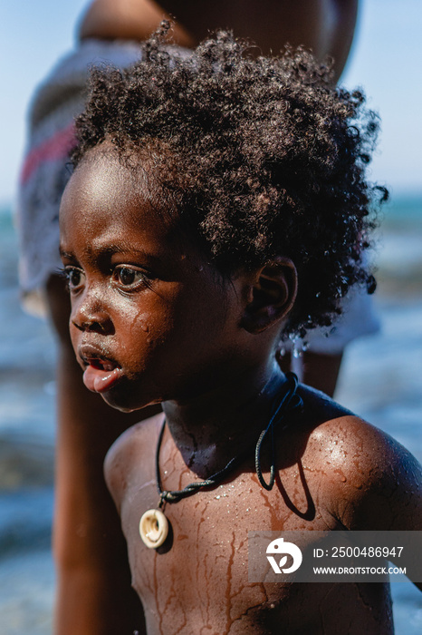 Retrato vertical del perfil de un pequeño niño afroamericano de cabello afro mojado en la playa en u