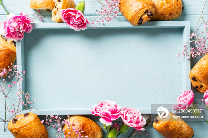 Holiday background with mini fresh croissants bun with chocolate and carnation flowers on blue turqu