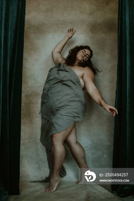 portrait of a plus size woman on tippy-toes reaching up covered in gray fabric