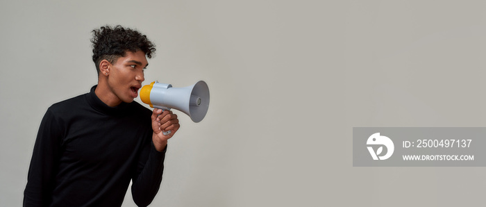 Stylish young guy with piercing dressed in black looking away and screaming in megaphone, making sal