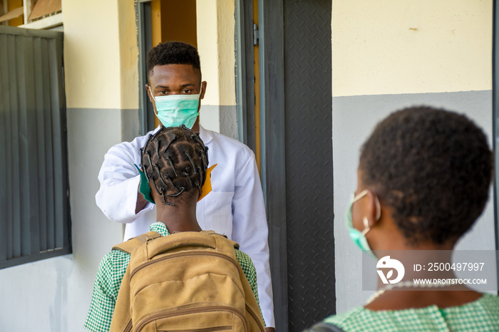 teacher in a school checking pupils body temperature before they enter the classroom