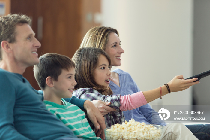 Family watching TV and eating popcorn on sofa