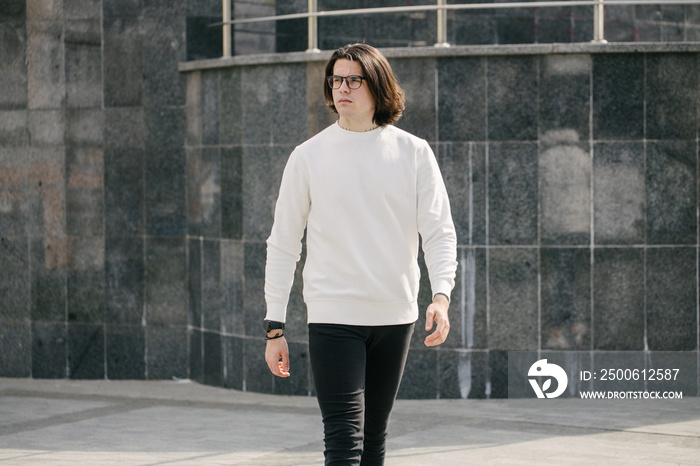 Man wearing blank white sweatshirt standing over gray background. Sweatshirt or hoodie for mock up, 