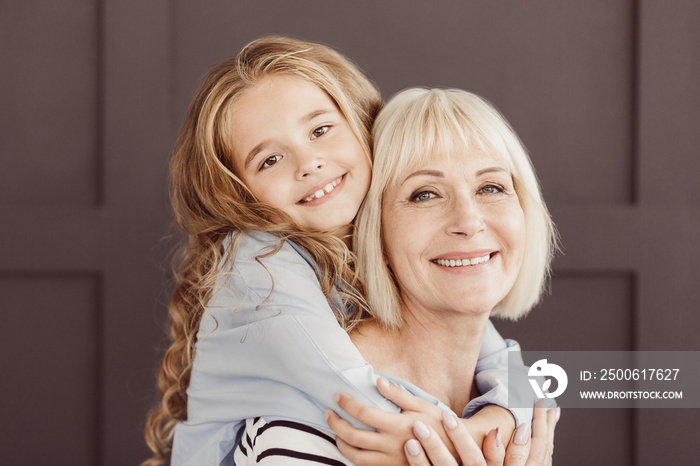 Happy grandmother and girl looking at camera over brown wall