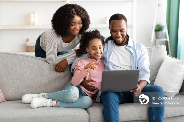 Happy black family of three using laptop in living room