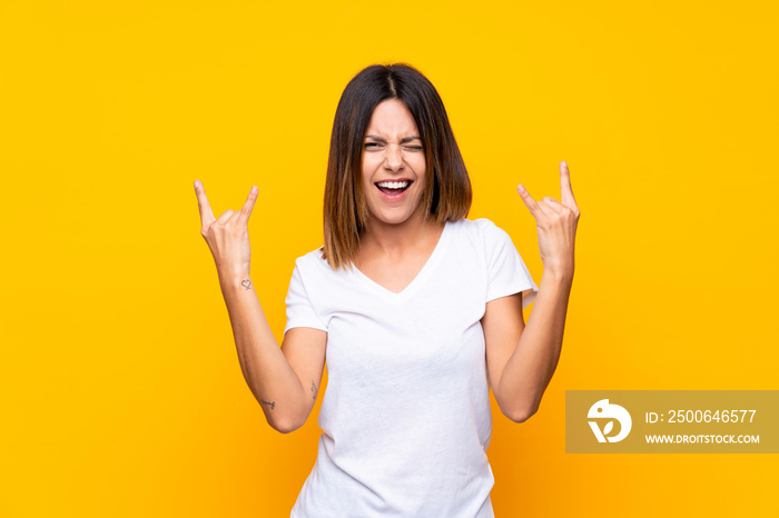 Young woman over isolated yellow background making rock gesture